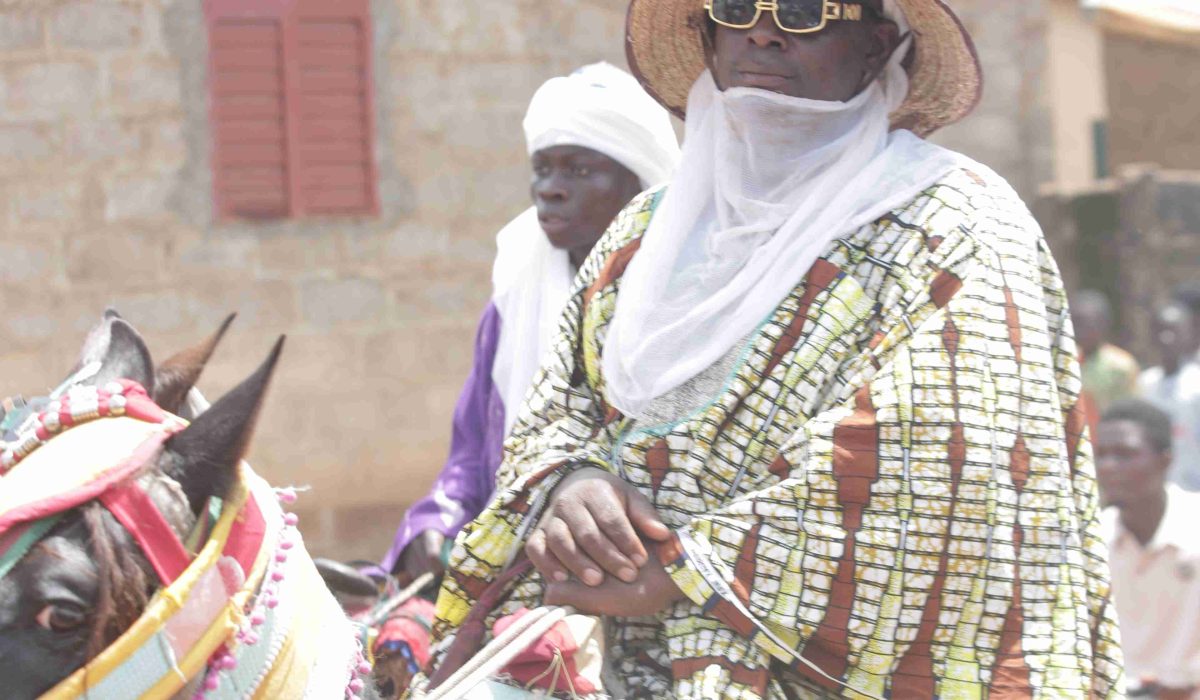Horseman wearing sunglasses and a traditional robe on his decorated horse, accompanied by another horseman in white.