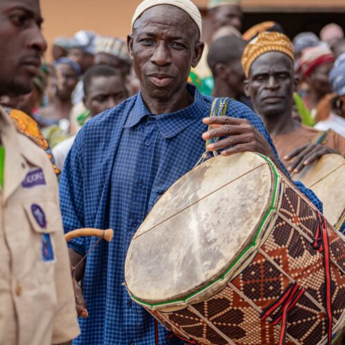 Homme jouant du tambour traditionnel, entouré de la foule pendant les festivités.